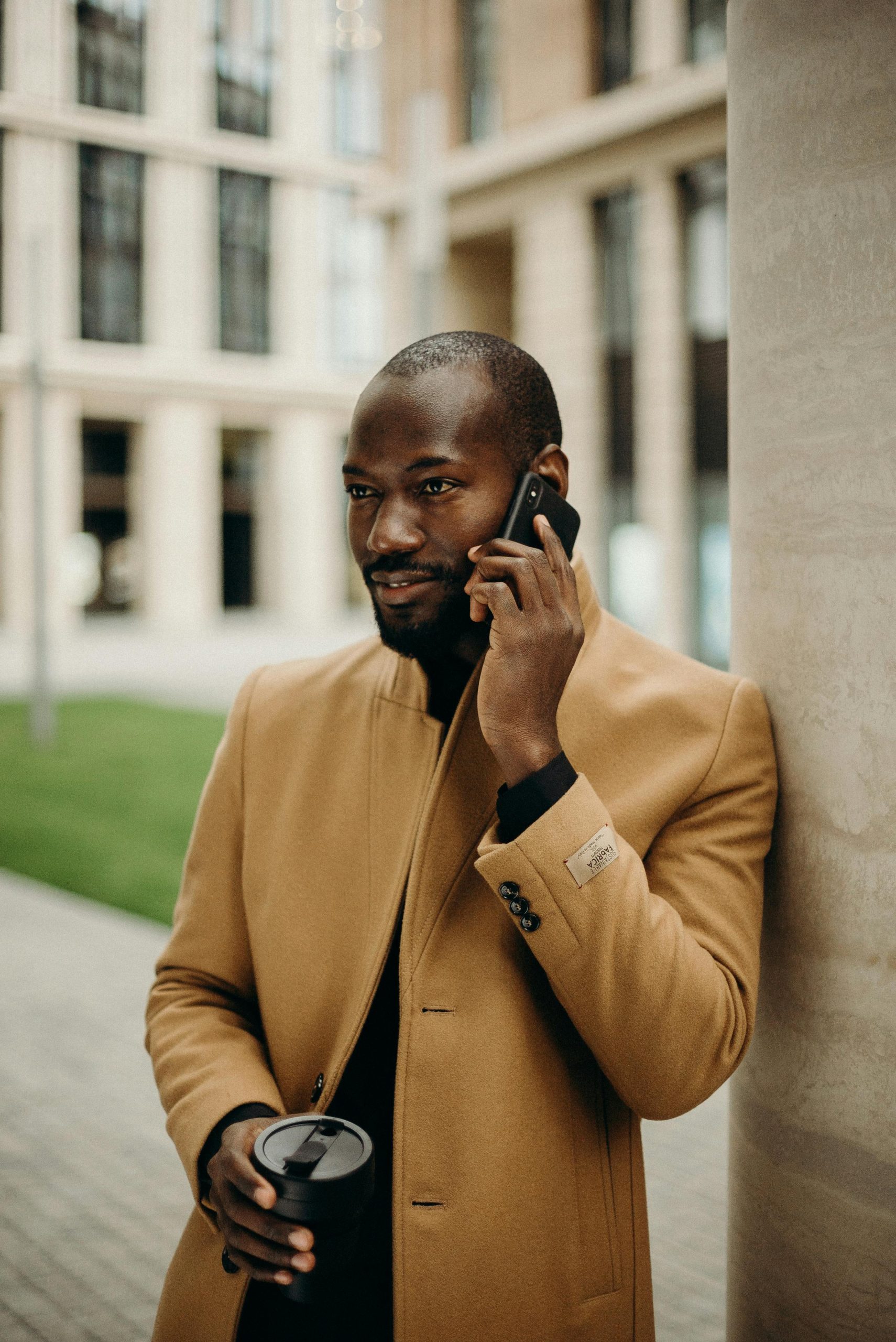 Elegant man in a trench coat talking on a smartphone outdoors.